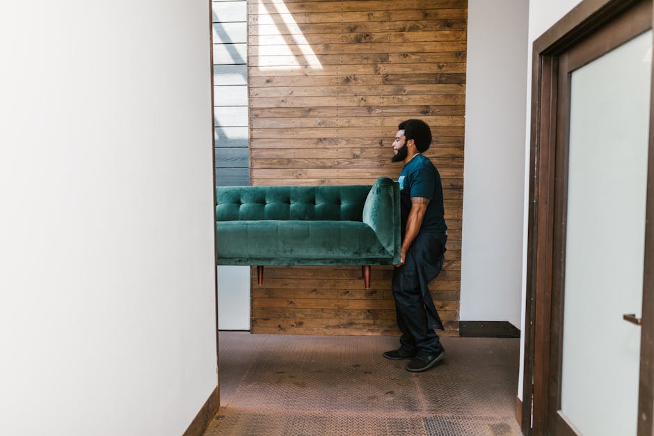 Two movers from [COMPANY_NAME] stand on a residential sidewalk in W2, London, during a home relocation process. One mover, an African descent man with a beard, wears a navy blue T-shirt and dark trous