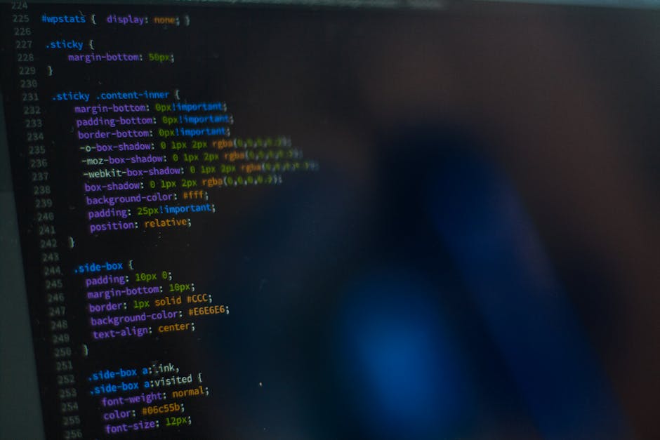 Close-up of a computer screen displaying a software development code editor with lines of programming code in various colours. The left side shows a directory structure with folders such as 'public,'